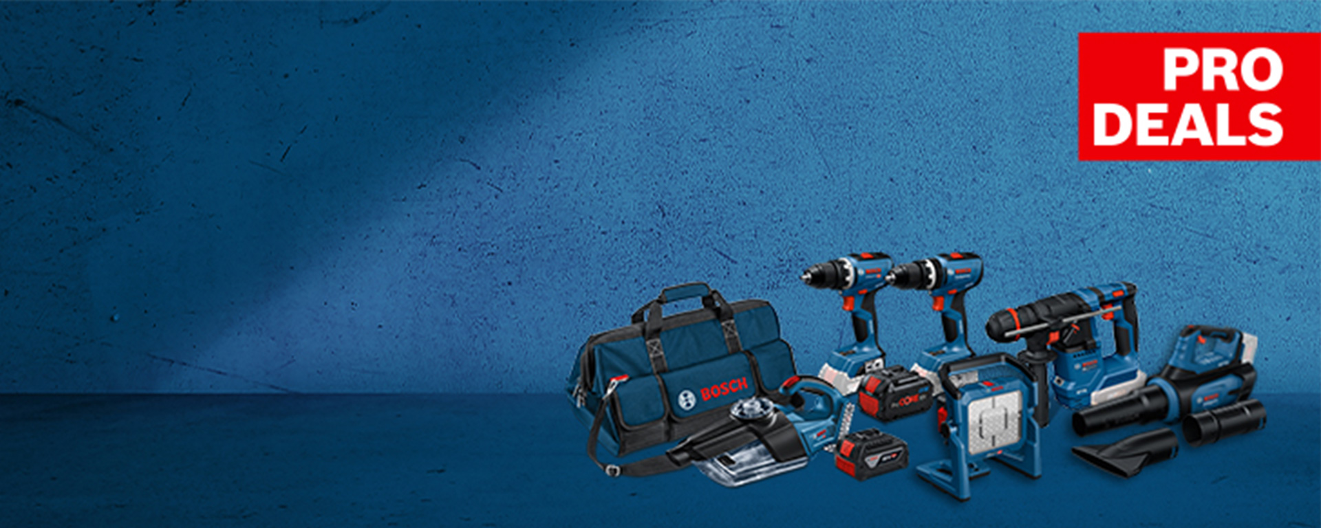 파란색 Bosch Professional 공구 가방이 단색 파란색 배경 위에 배터리로 작동하는 다양한 공구들, 예를 들어 배터리 드릴, 배터리 드라이버 및 배터리 해머 드릴 옆에 놓여 있습니다. 오른쪽 상단에는 흰색으로 'PRO DEALS'라고 적혀 있습니다.