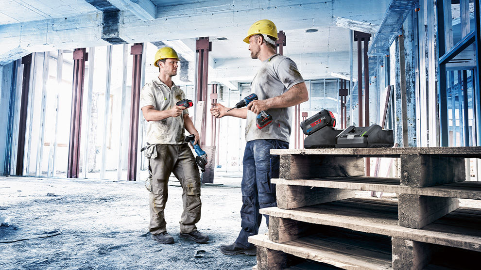두 건설 노동자가 보쉬 도구를 들고 나무 팔레트 위에 서 있습니다.