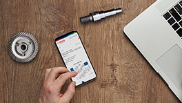 나무 테이블 위에 스마트폰이 있고, 그 옆에 노트북 키보드와 도구가 있습니다.