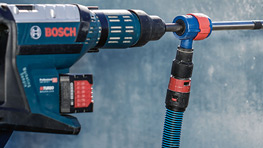 회색 벽에 빨간색과 검은색 드릴이 있는 파란색 Bosch 도구의 클로즈업.