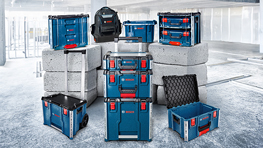 회색 배경에 빨간색 강조가 있는 파란색 공구 상자의 배열, 콘크리트 블록으로 둘러싸여 있습니다. 배경에 배낭이 보입니다.