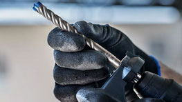 검은 장갑을 낀 손이 Bosch Professional의 드릴을 들고 있습니다.