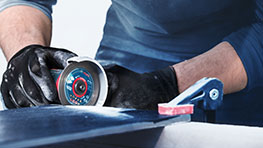 장갑을 낀 사람이 Bosch Professional 연마기로 자르고 있습니다.