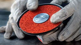 작업 장갑을 낀 손이 빨간 연마 디스크를 잡고 있습니다.