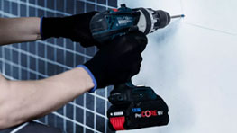검은 장갑을 낀 사람이 Bosch 무선 드릴로 벽에 구멍을 뚫고 있습니다.