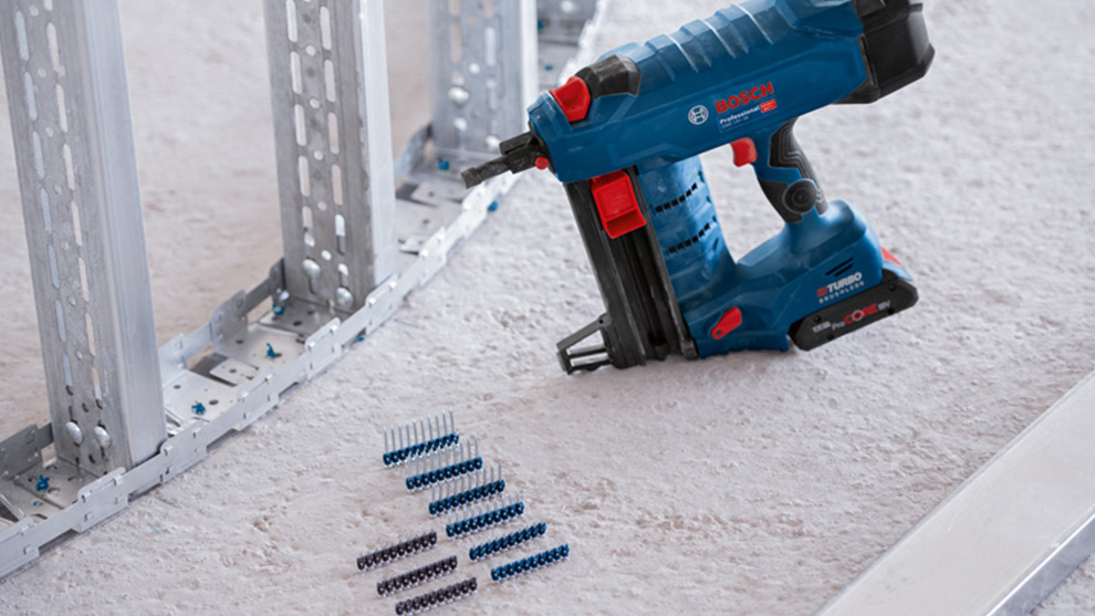 파란색 Bosch Professional 배터리 못 박는 기계가 카펫 위의 나사 옆에 놓여 있습니다.