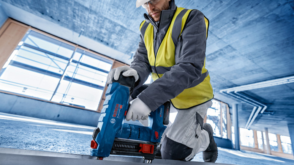 안전 조끼를 입은 남성이 파란색 Bosch 배터리 못 박기를 사용하고 있습니다.