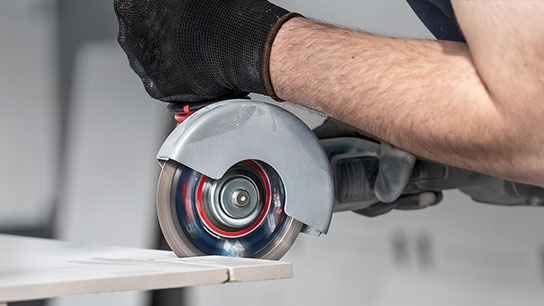 검은 장갑을 낀 손이 회색 Bosch Professional 절단톱을 잡고 있습니다.