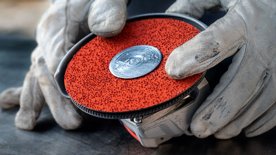 장인이 도구에 빨간 점이 있는 연마 디스크를 부착하고 있습니다.