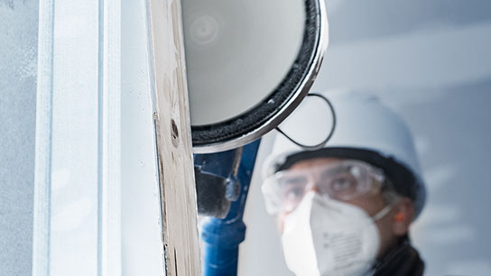 보호 마스크와 헬멧을 쓴 작업자가 롤러로 벽을 칠하고 있습니다.