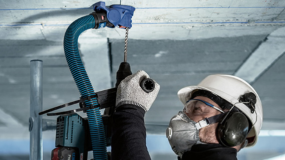 헬멧과 귀 보호구를 착용한 장인이 천장을 뚫고 있습니다.