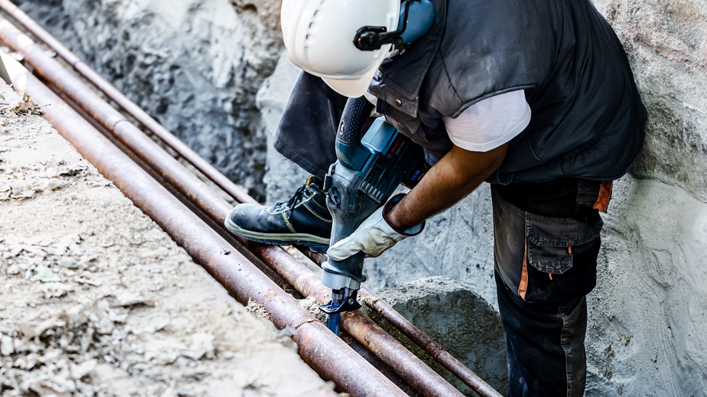 헬멧을 쓴 작업자가 Bosch 도구로 파이프를 자르고 있습니다.