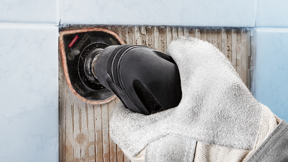 장갑을 낀 손이 타일 위에 보쉬 도구를 들고 있습니다.