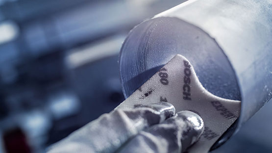 장갑을 낀 손이 금속 파이프에 사포를 대고 있습니다.