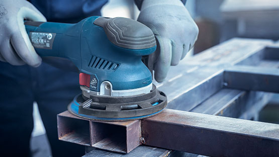 파란색 Bosch Professional 편심 샌더가 금속 표면에 사용됩니다.