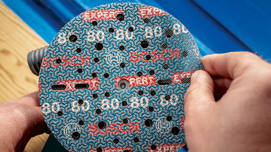 한 손이 구멍이 있는 파란색 Bosch 연마 디스크를 들고 있습니다.