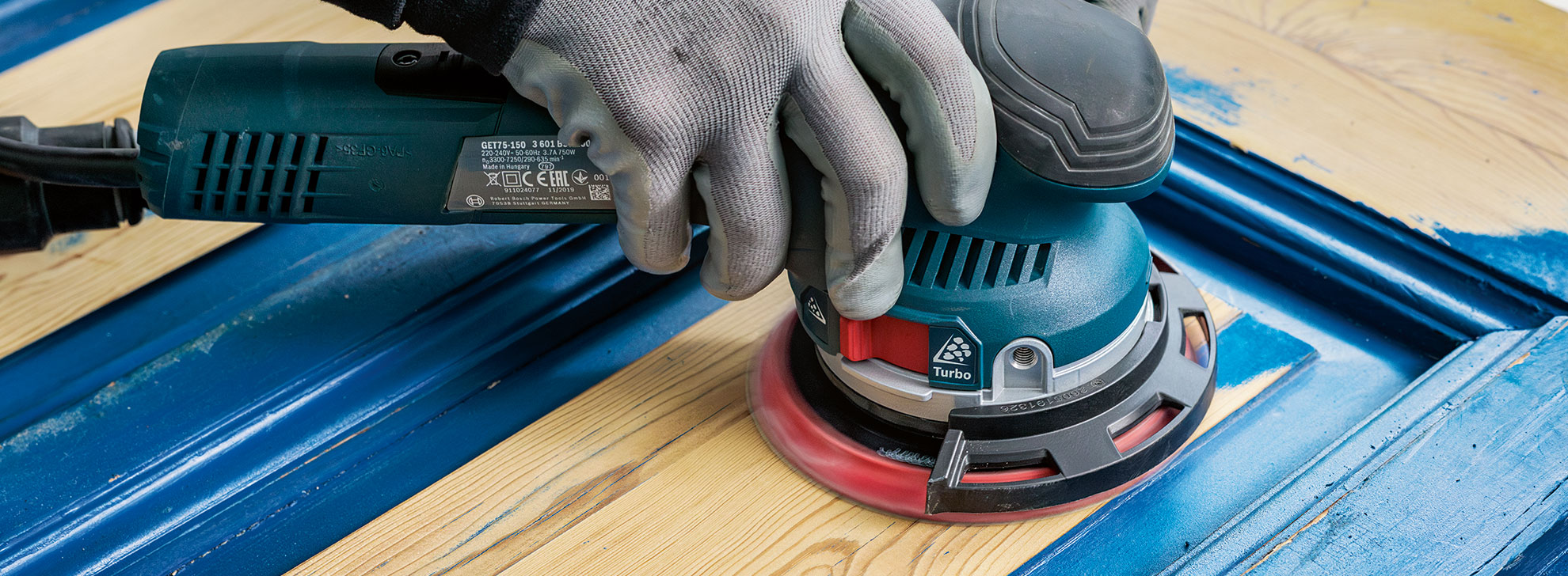 한 손이 나무 위에서 Bosch Professional 편심 샌더를 사용하고 있습니다.