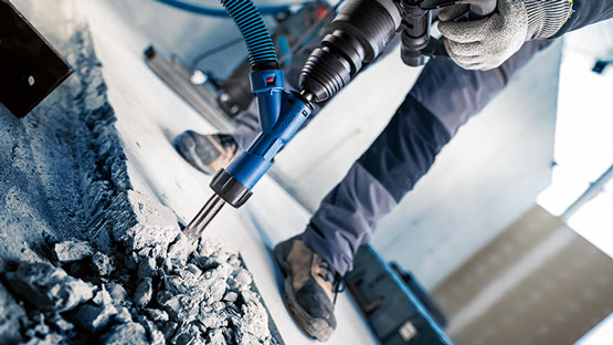 보쉬 프로페셔널 드릴이 콘크리트 바닥을 작업하고 있으며, 작업 장갑을 낀 작업자입니다.