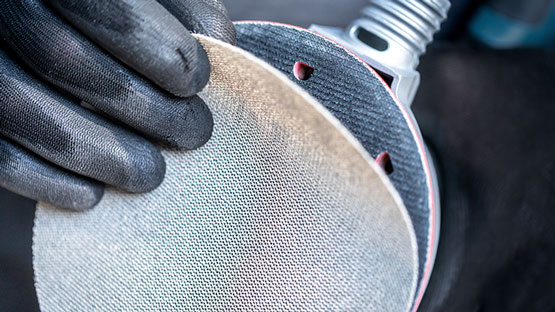 한 사람이 검은 장갑을 끼고 구멍이 있는 연마판을 들고 있습니다.