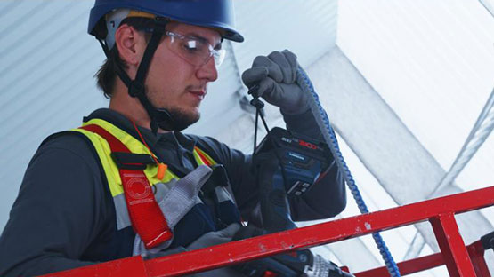 안전복을 입은 작업자가 사다리에서 Bosch 도구를 사용하고 있습니다.