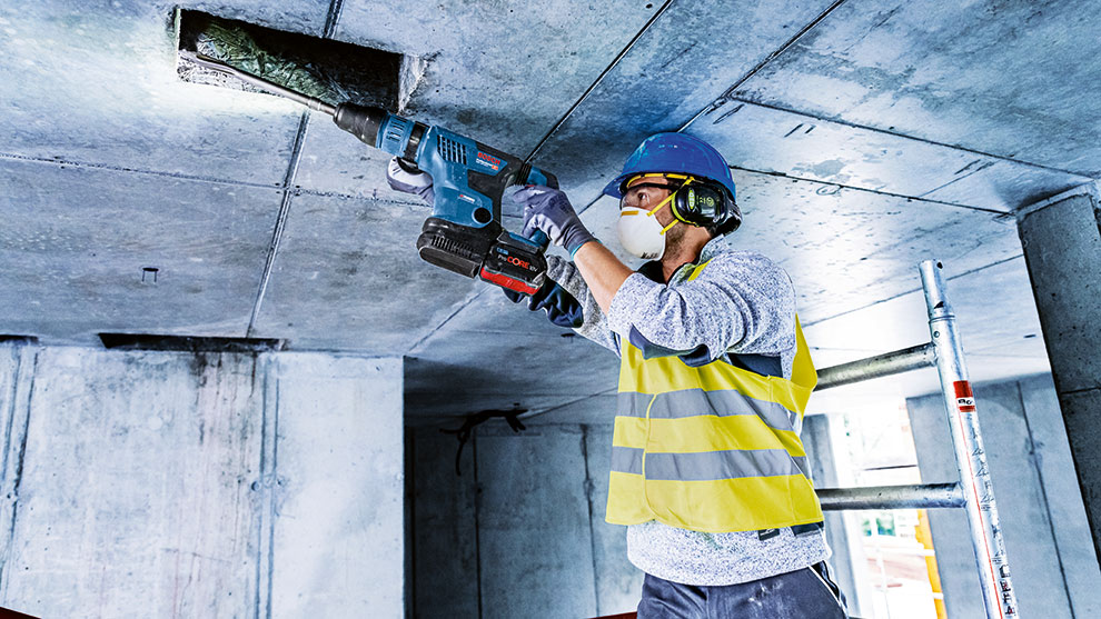 안전모를 쓴 작업자가 파란색 Bosch Professional 도구로 구멍을 뚫고 있습니다.