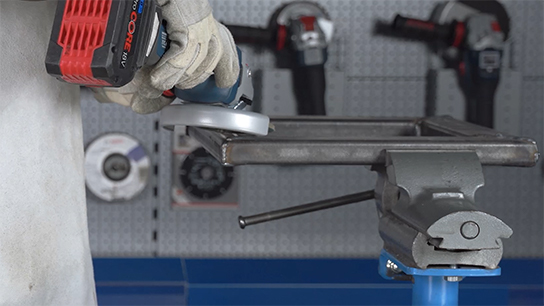 한 사람이 작업물 위에 Bosch Professional 앵글 그라인더를 들고 있습니다.