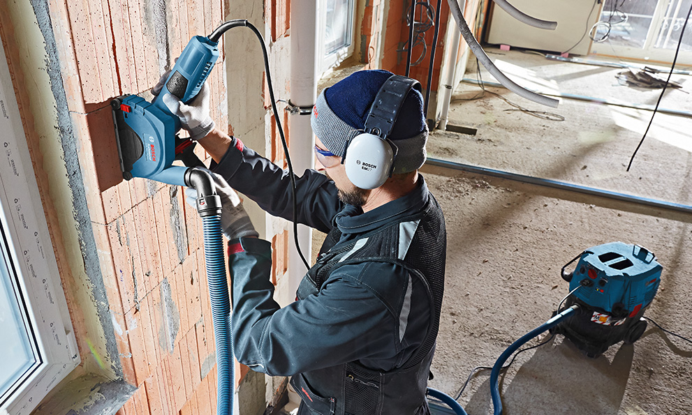 귀 보호구를 착용한 남성이 벽에서 Bosch Professional 도구를 사용하고 있습니다.