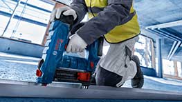 한 장인이 건설 현장에서 파란색 Bosch 배터리 못 박는 기계를 사용하고 있습니다.