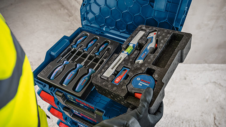 파란색 Bosch Professional 공구 상자가 다른 가방 위에 놓여 있으며, 두 개 모두 빨간 잠금 장치가 있습니다. 바닥은 회색입니다.