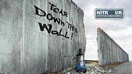 회색 벽에 "Tear Down The Wall!"라는 그래피티와 파란 크레인이 있습니다.
