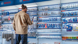 한 남자가 파란색과 흰색 포장으로 배열된 Bosch Professional 도구가 있는 선반 앞에 서 있습니다.