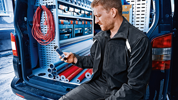 검은 옷을 입은 장인이 밴에 앉아 휴대폰을 사용하고 있습니다.