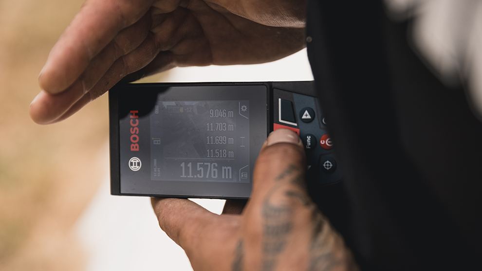 한 손이 디스플레이가 있는 Bosch Professional 레이저 거리 측정기를 들고 있습니다.