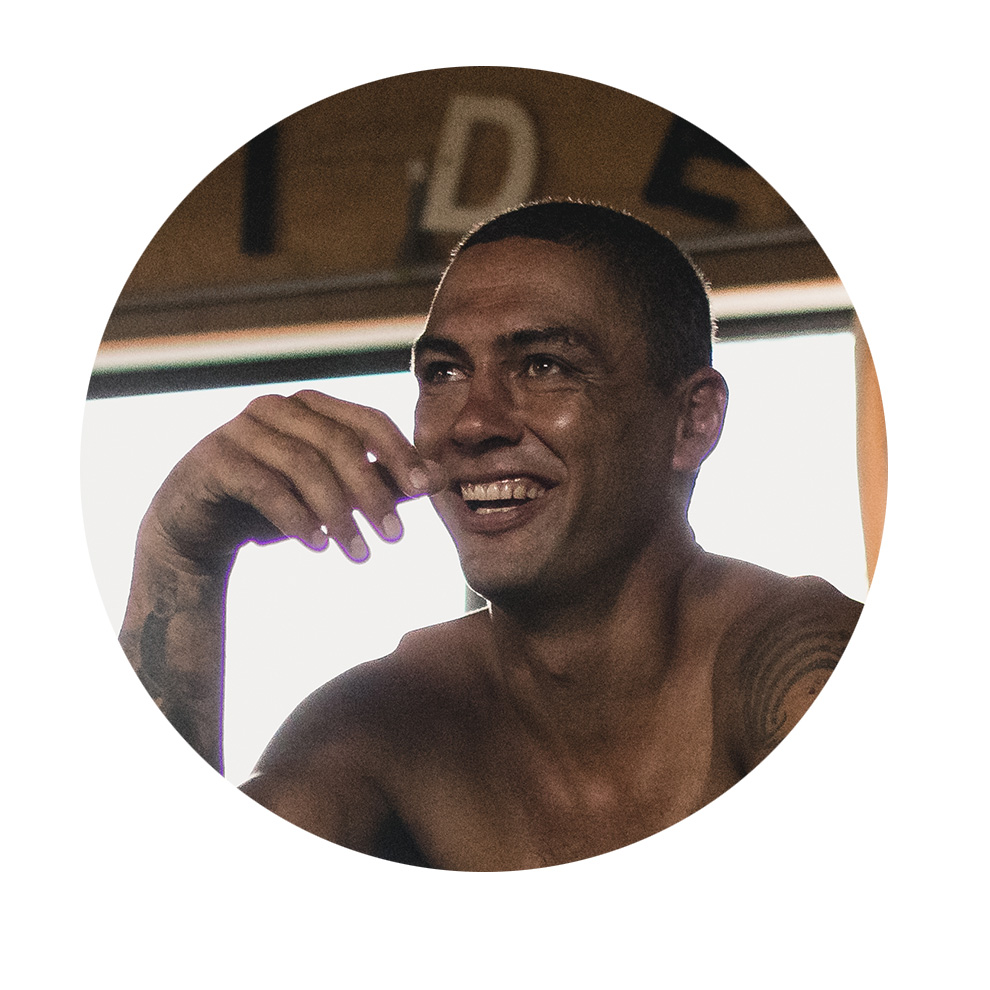 문신을 한 웃고 있는 남자가 밝은 방에 앉아 있습니다.