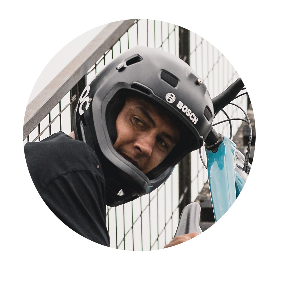 검은색 Bosch 헬멧을 쓴 남자가 카메라를 바라보며 자전거를 들고 있습니다.