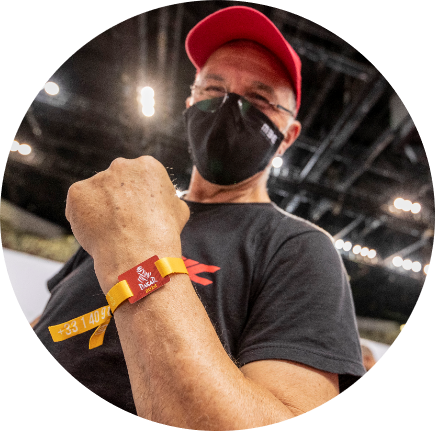 마스크를 쓴 남자가 그의 다채로운 팔찌를 보여주며 미소 짓고 있습니다.