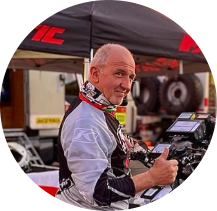 레이싱 복장을 한 남자가 텐트와 오토바이 앞에서 엄지손가락을 올리고 있습니다.