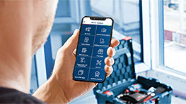 한 남자가 손에 앱이 있는 스마트폰을 들고 있으며, 배경에는 여행 가방이 있습니다.